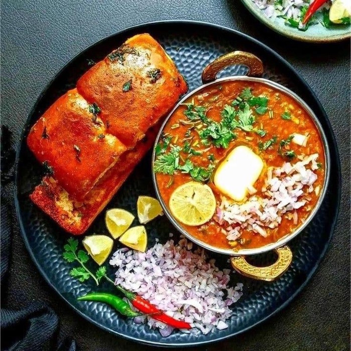 Paav bhaji with buttered pav, onions and lime on a black plate